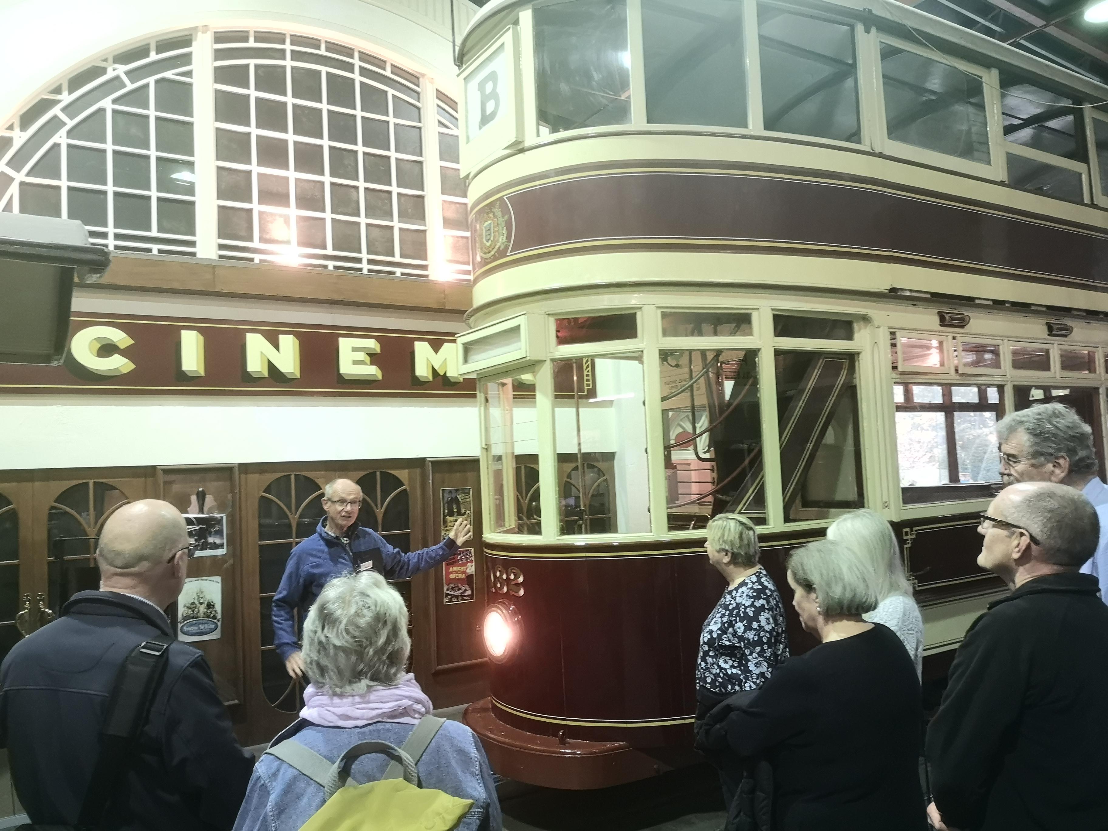 A man talking to a group while stood in front of a red and cream trolleybus.